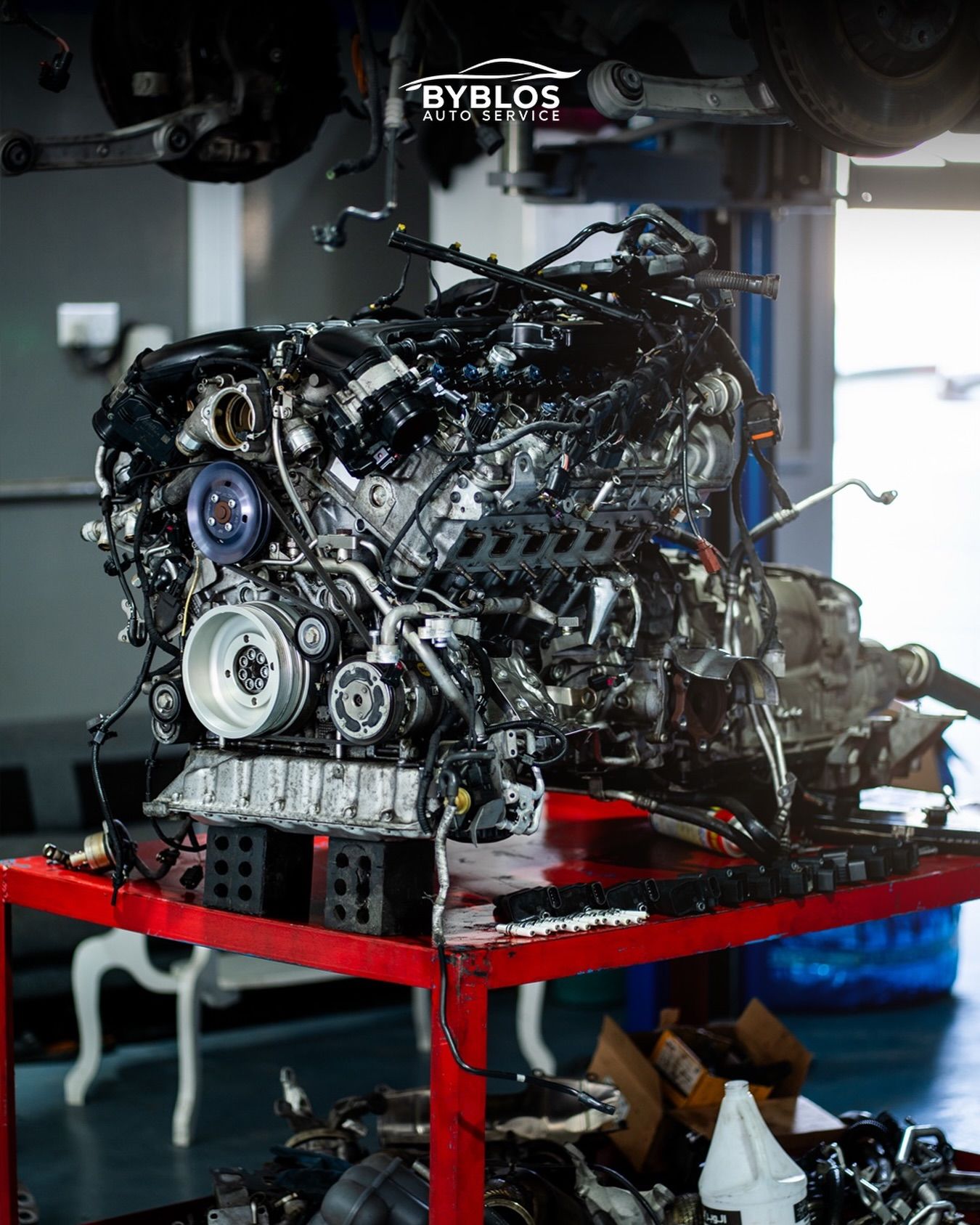 An engine out of its car on a red stand in the BYBLOS workshop, with the gearbox still attached