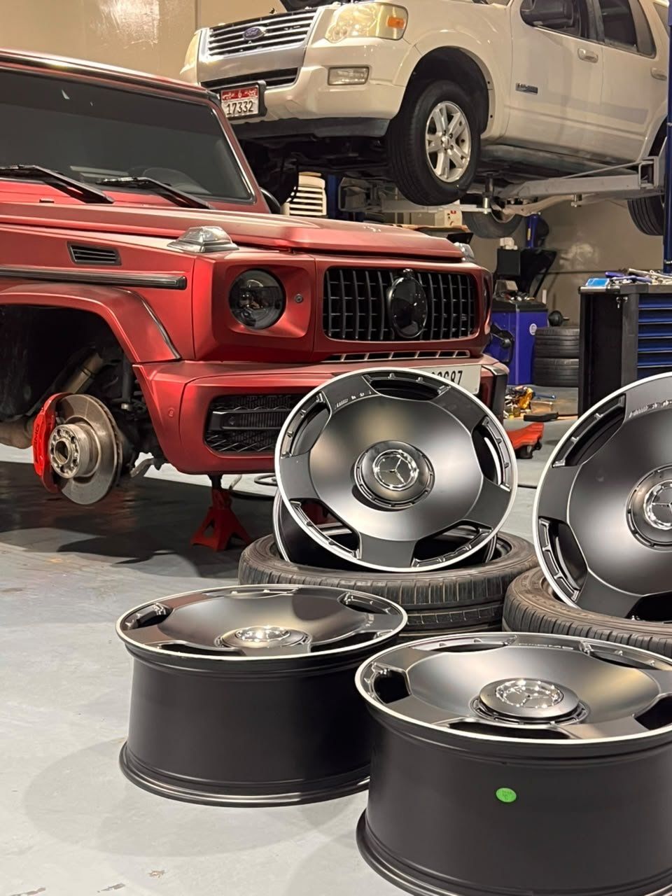 Red Mercedes G 63 on stands, new black wheels stacked in front of it