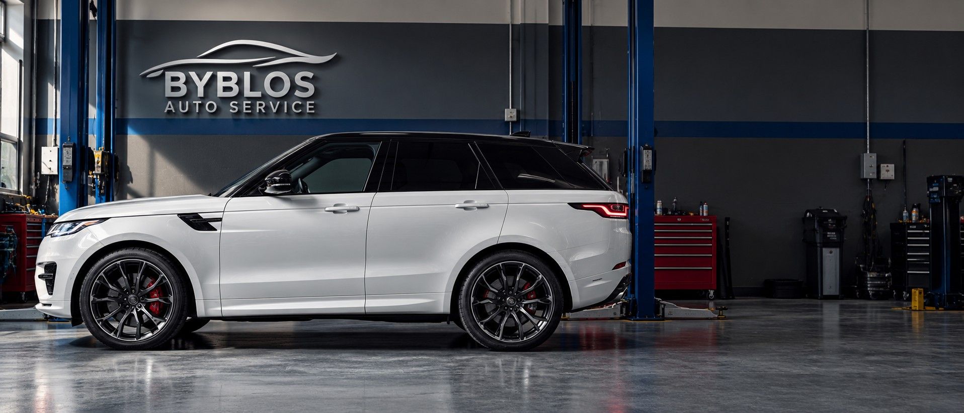 A white Range Rover Sport parked in the BYBLOS workshop, blue lifts and the BYBLOS sign on the wall behind it